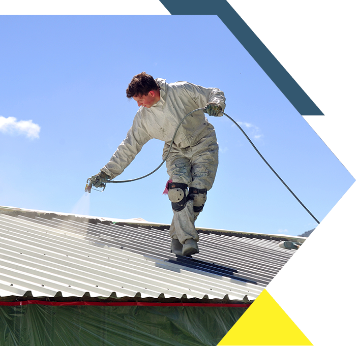 Worker spray painting on a metal roof.